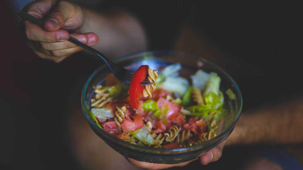 A vibrant bowl of healthy pasta salad with fresh vegetables in a casual setting.